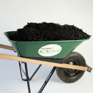 A green wheelbarrow with dark brown mulch and the name Modern Turf with logo sticker on the side of the wheelbarrow A green wheelbarrow with dark brown mulch and the name Modern Turf with logo sticker on the side of the wheelbarrow