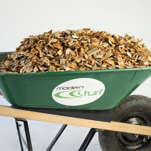A green wheelbarrow filled with wood chips, labeled modern turf, on a white background.