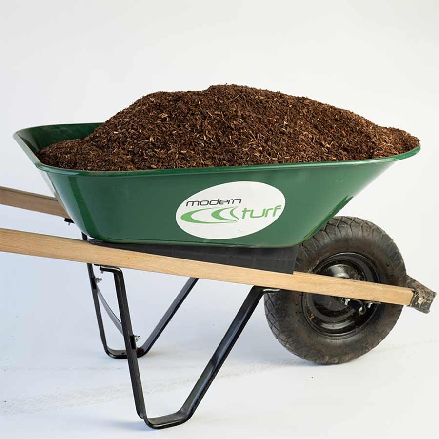 Green wheelbarrow filled with dark brown mulch, raised on its legs against a plain white background.