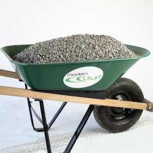 Green wheelbarrow filled with gravel, labeled modern turf, on a white background.