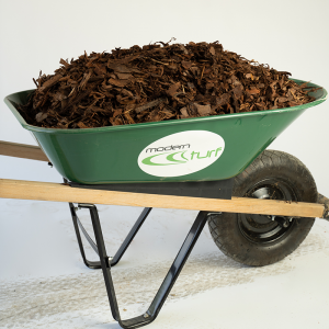 Green wheelbarrow full of mulch with modern turf logo, standing on a white surface.