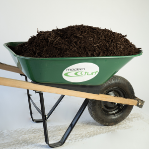 Green wheelbarrow filled with dark mulch, labeled modern turf, on a white background.